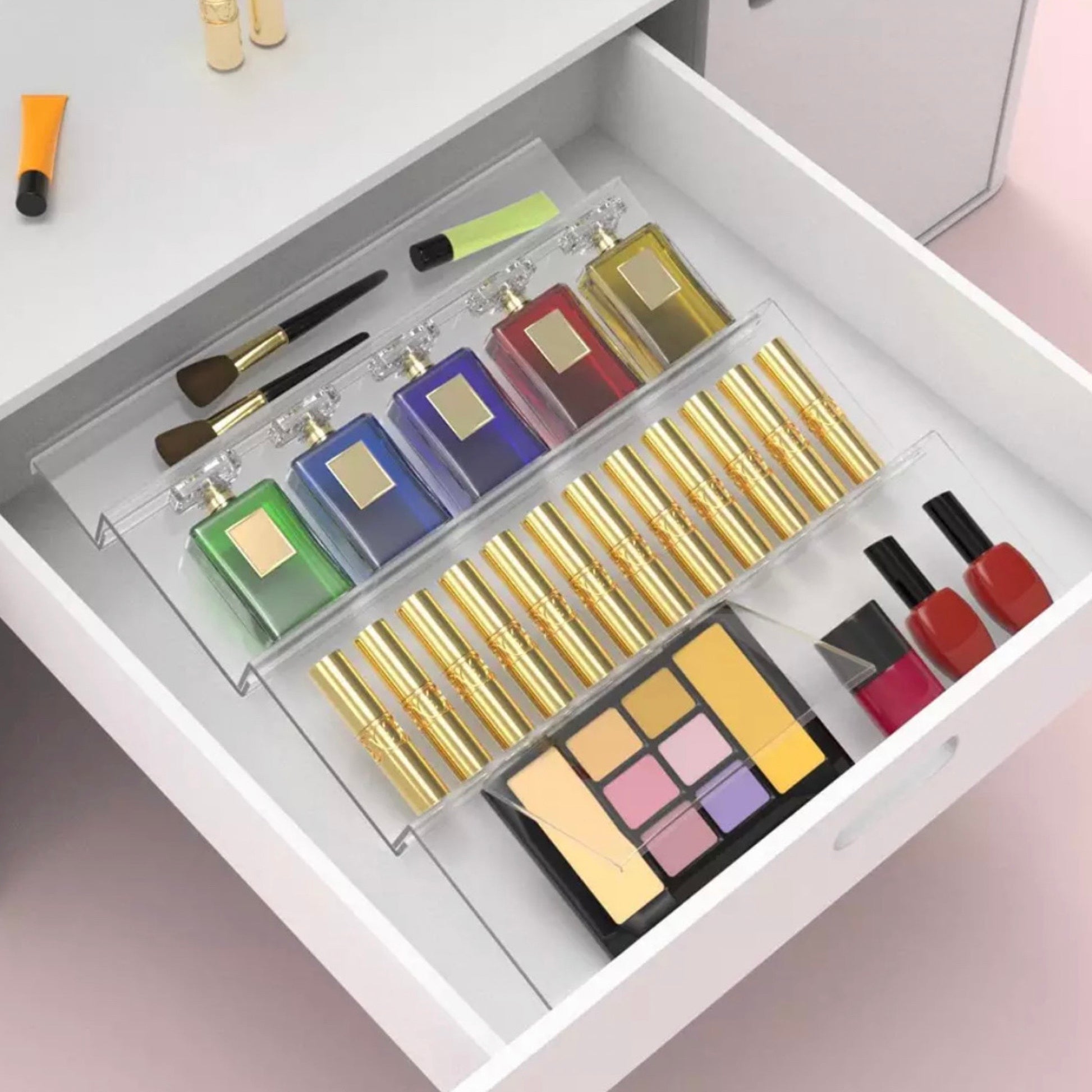 Innenansicht einer Schublade mit einem transparenten Acryl-Make-up-Organizer, der verschiedene Kosmetikprodukte farbenfroh und ordentlich anordnet. Zu sehen sind bunte Lidschattenpaletten, mehrere Lippenstifte in goldglänzenden Hülsen, Nagellack in Rot- und Rosatönen sowie Make-up-Pinsel. Dieses Aufbewahrungssystem bietet eine klare und attraktive Darstellung der Kosmetikartikel, erleichtert die Auswahl und hält die Produkte griffbereit.