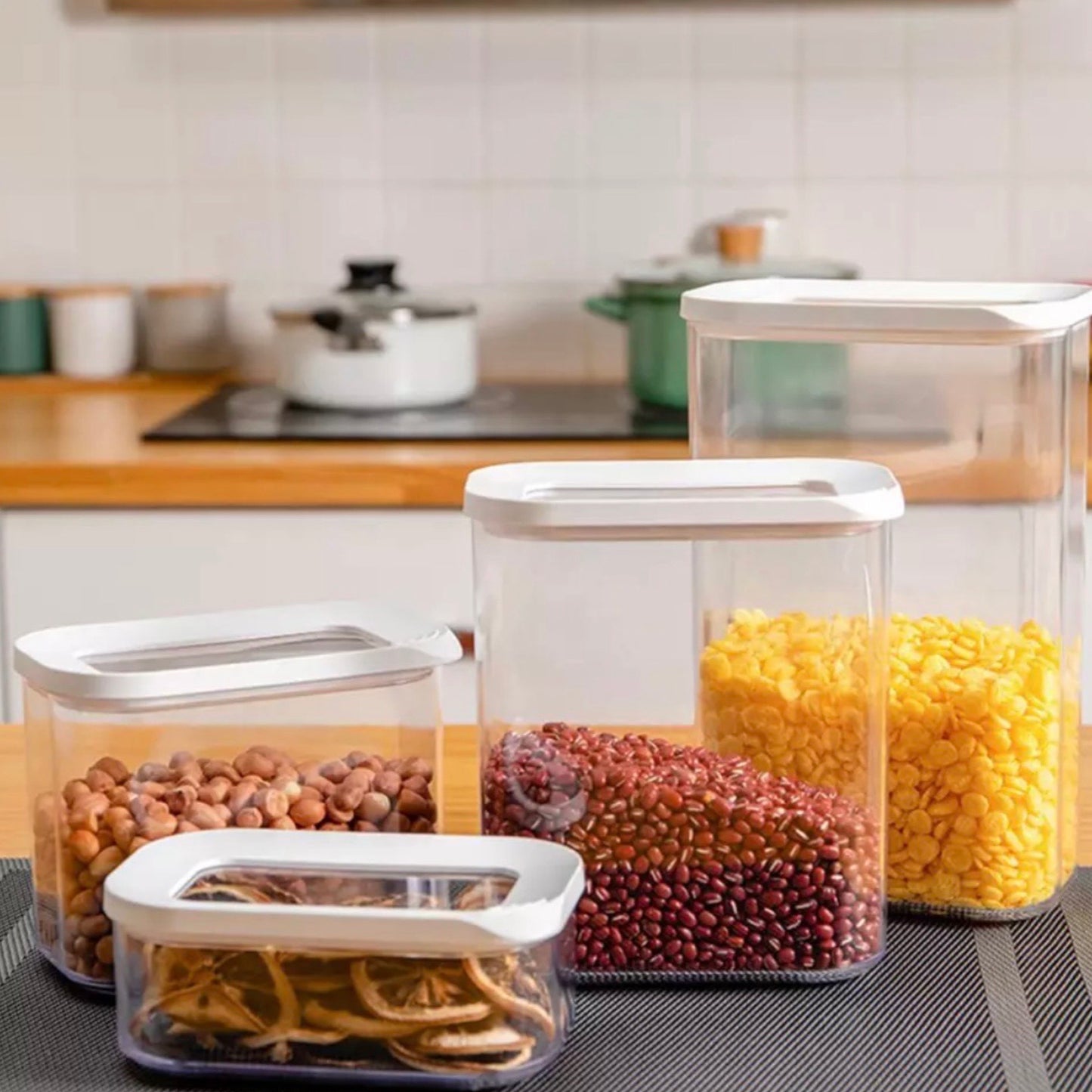 Set aus durchsichtigen Vorratsdosen in verschiedenen Größen auf einer Küchenarbeitsplatte, gefüllt mit Hülsenfrüchten und getrockneten Zitronenscheiben. Diese Behälter bieten eine klare Sicht auf ihren Inhalt und sind ideal zur übersichtlichen Aufbewahrung in der Küche