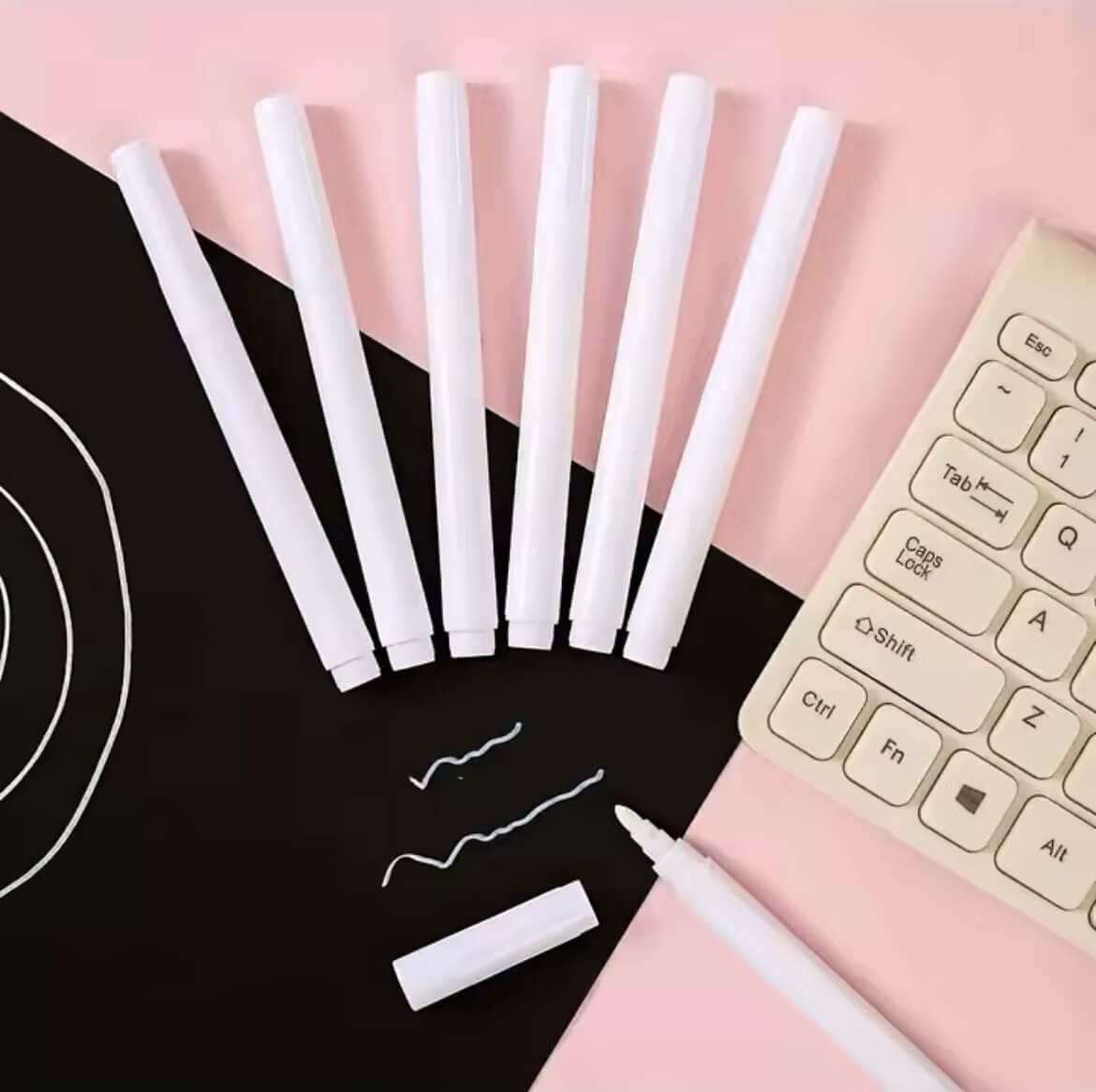 Weißer Kreidemarker , auf einem schwarzen und rosa Untergrund neben einer Tastatur arrangiert – ideal für glatte Oberflächen wie Glas, Tafeln oder Etiketten.