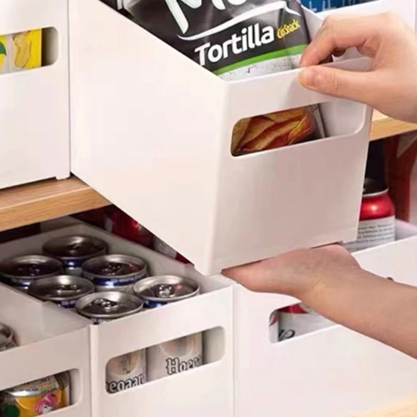 Eine stapelbare Aufbewahrungsbox mit Griff, hier als praktische Lösung zur Aufbewahrung von Lebensmitteln im Schrank gezeigt. Die obere Schublade ist geöffnet und enthält eine Packung Tortillachips, während die unteren Fächer mit Konservendosen bestückt sind. Diese weißen Organizer-Boxen eignen sich hervorragend zur übersichtlichen und platzsparenden Lagerung in der Küche.