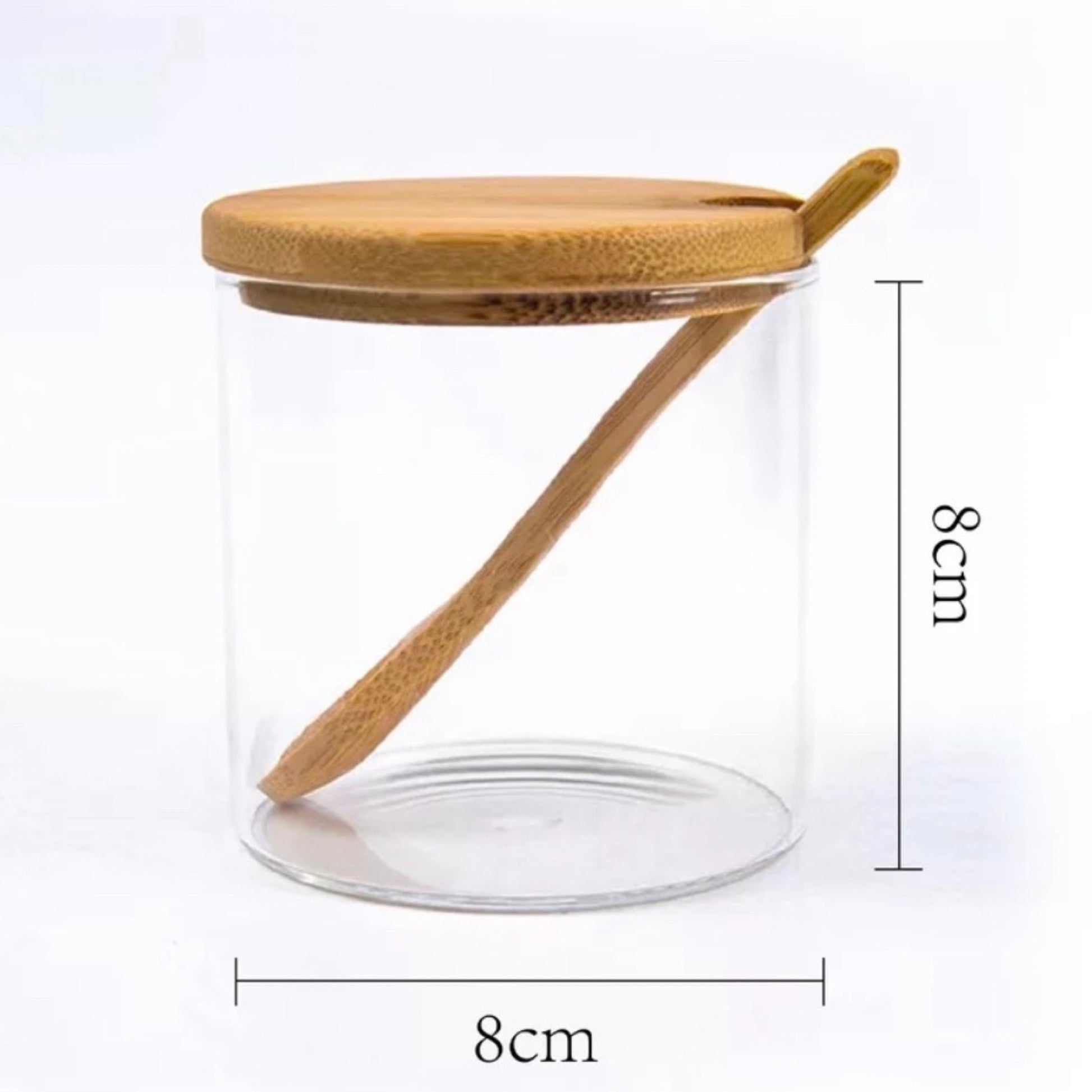Ein klares, zylindrisches Gewürzglas mit einem Bambusdeckel und einem passenden Bambuslöffel, der sich über die Länge des Glases erstreckt. Die Dimensionen des Glases sind gleichmäßig mit einer Höhe und Breite von jeweils 8 cm angegeben, was eine perfekte Würfelgeometrie suggeriert. Der Fokus liegt auf der Einfachheit und den natürlichen Materialien.