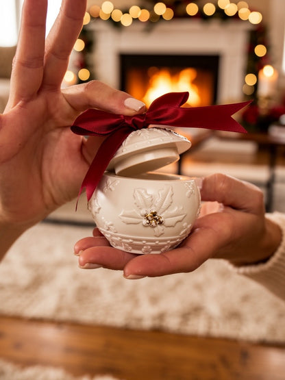 Geöffneter handgefertigter Weihnachtskerzenhalter in Kugelform mit roter Schleife, festlich vor Kaminfeuer präsentiert.