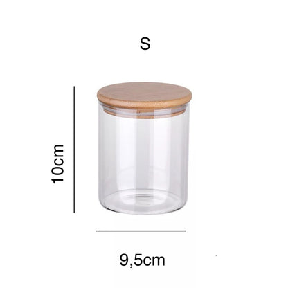 Ein kleines transparentes Vorratsglas mit den Maßen 10 cm Höhe und 9,5 cm Durchmesser, gekrönt von einem glatten Bambusdeckel. Dieses Glas ist ideal für die platzsparende und sichtbare Aufbewahrung von kleinen Küchenzutaten oder Bürobedarf und fügt sich nahtlos in jede moderne oder traditionelle Einrichtung ein.