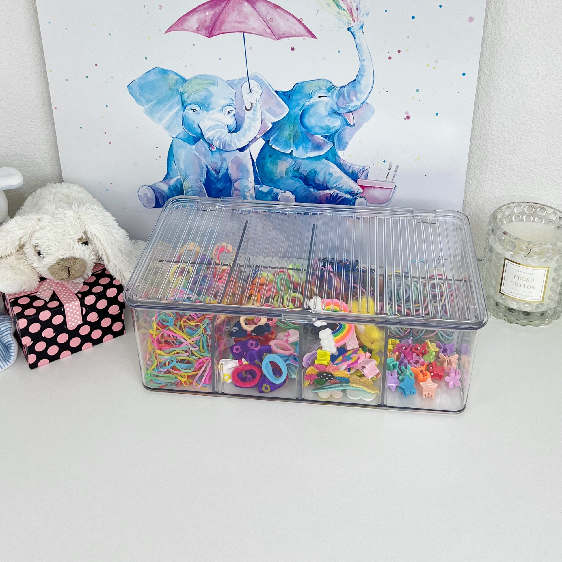 Transparente Aufbewahrungsbox mit Deckel und mehreren Fächern, gefüllt mit bunten Haargummis, Clips und kleinen Accessoires – ideal zum Organisieren im Kinderzimmer.