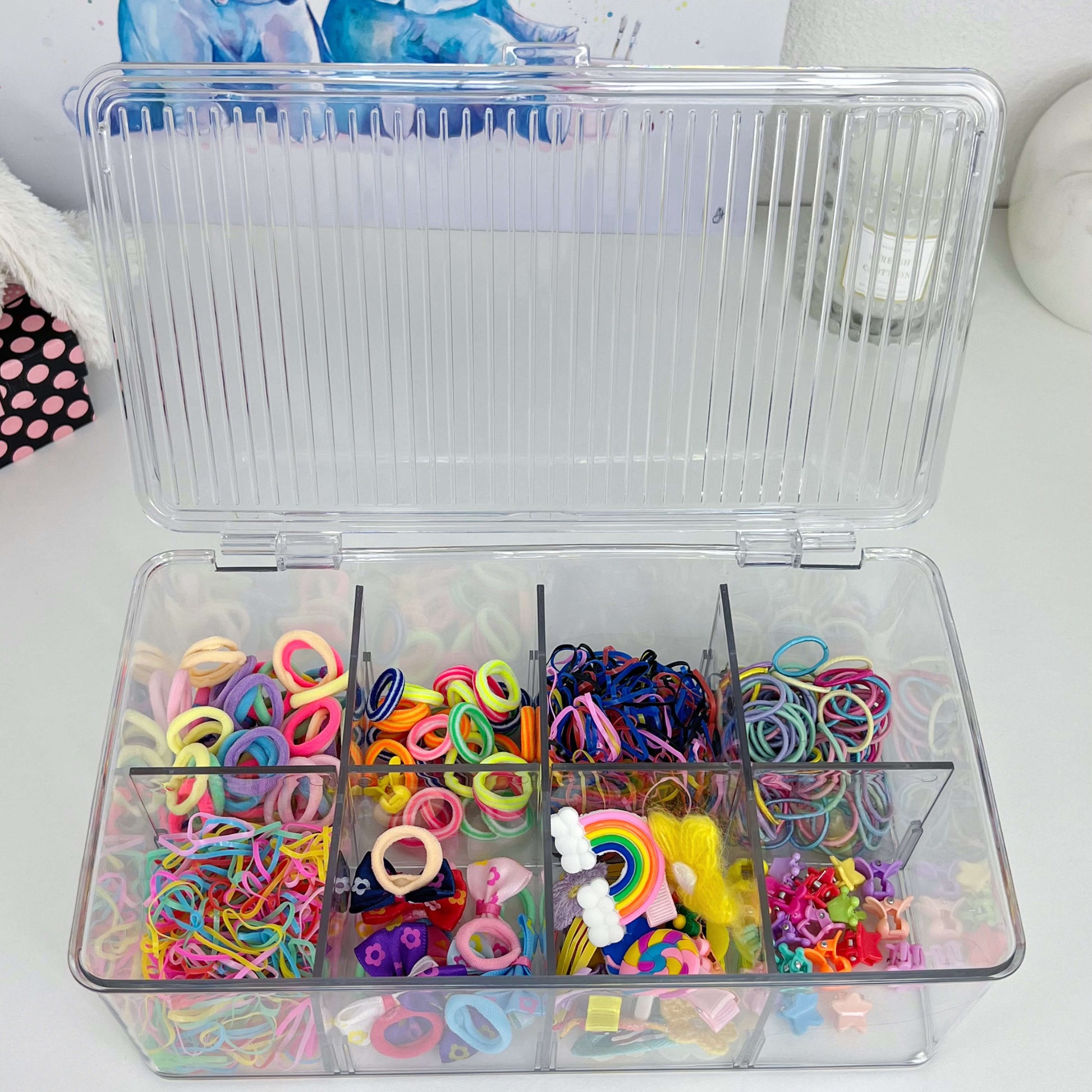 Transparenter Schubladen-Organizer mit mehreren Fächern, gefüllt mit bunten Haargummis, Clips und Accessoires – praktische Aufbewahrung für Kinderzimmer oder Badezimmer.