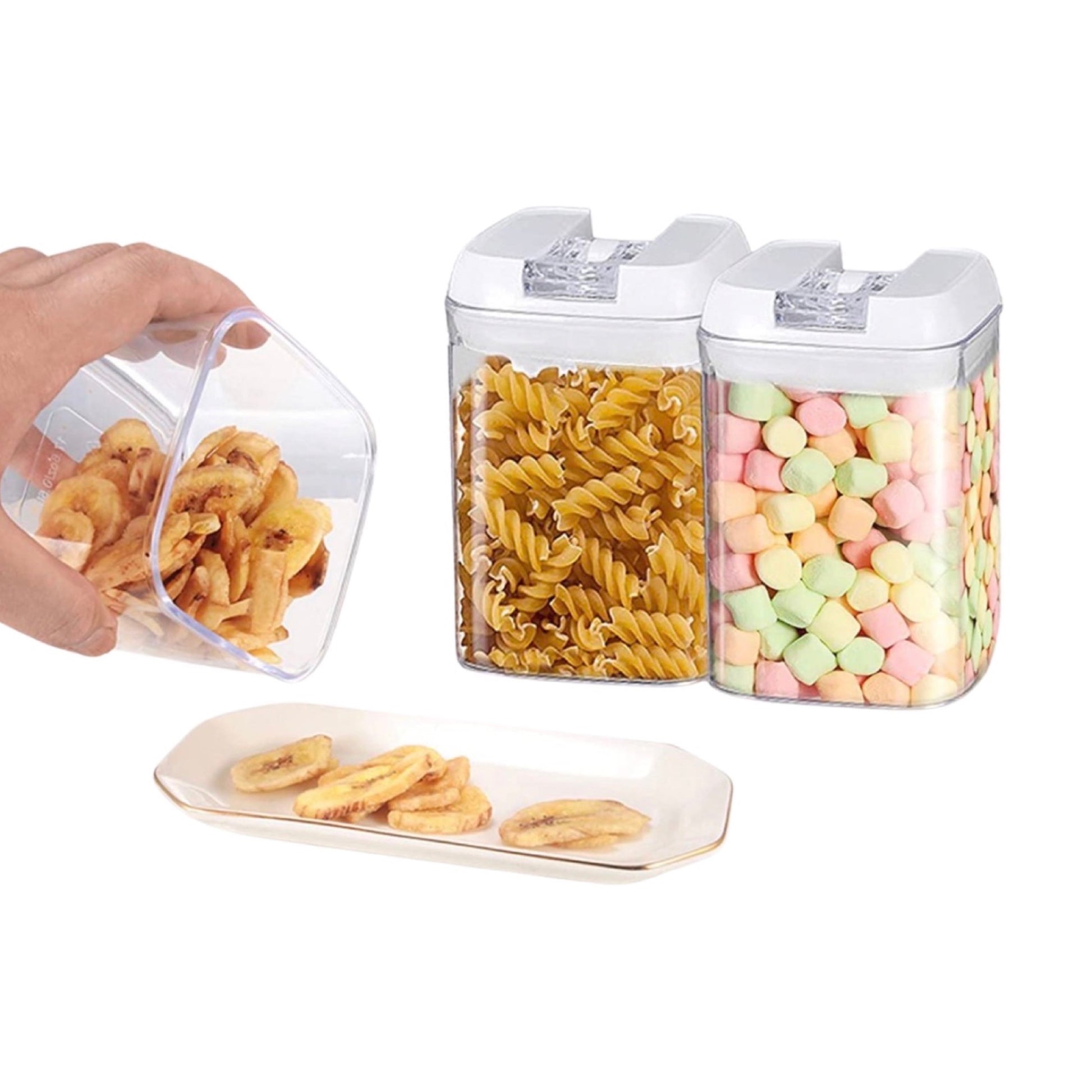 Eine Hand hält einen transparenten Behälter, aus dem getrocknete Bananenchips auf einen weißen Teller gegossen werden, neben zwei weiteren versiegelten Behältern mit Fusilli-Nudeln und bunten Marshmallows, die die Praktikabilität und Benutzerfreundlichkeit der Vorratsbehälter für verschiedene Lebensmittel demonstrieren.