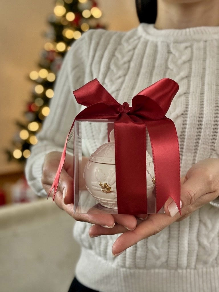 Hand hält handgefertigten Weihnachtskerzenhalter in transparenter Geschenkbox mit roter Schleife – festliche Deko aus der Schweiz
