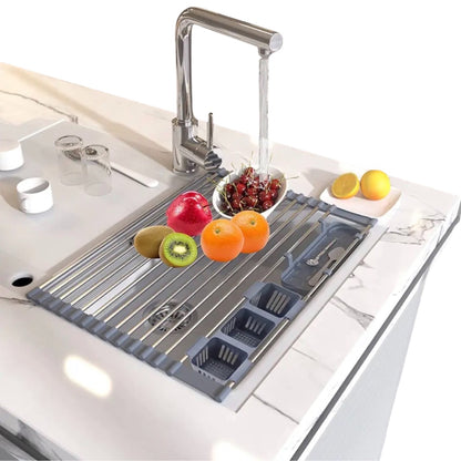 Modernes Abtropfgestell aus Edelstahl über einem Küchenspülbecken mit laufendem Wasserhahn, ausgestattet mit einem Besteckhalter und rutschfesten Silikonenden. Frische Früchte wie Kiwis, Orangen, und ein Granatapfel befinden sich auf dem Gestell neben einem Teller mit halbierter Zitrone und zwei Gläsern.