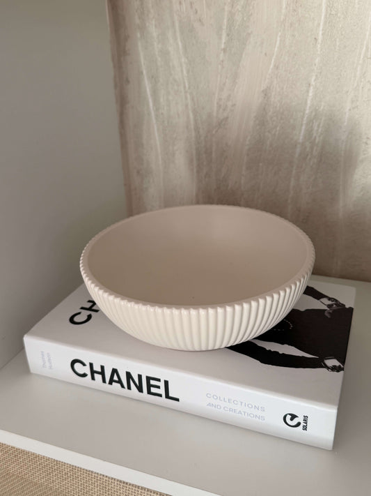Cremeweiße, handgefertigte Schale auf einem Chanel-Buch, dekorativ präsentiert als modernes Wohnaccessoire