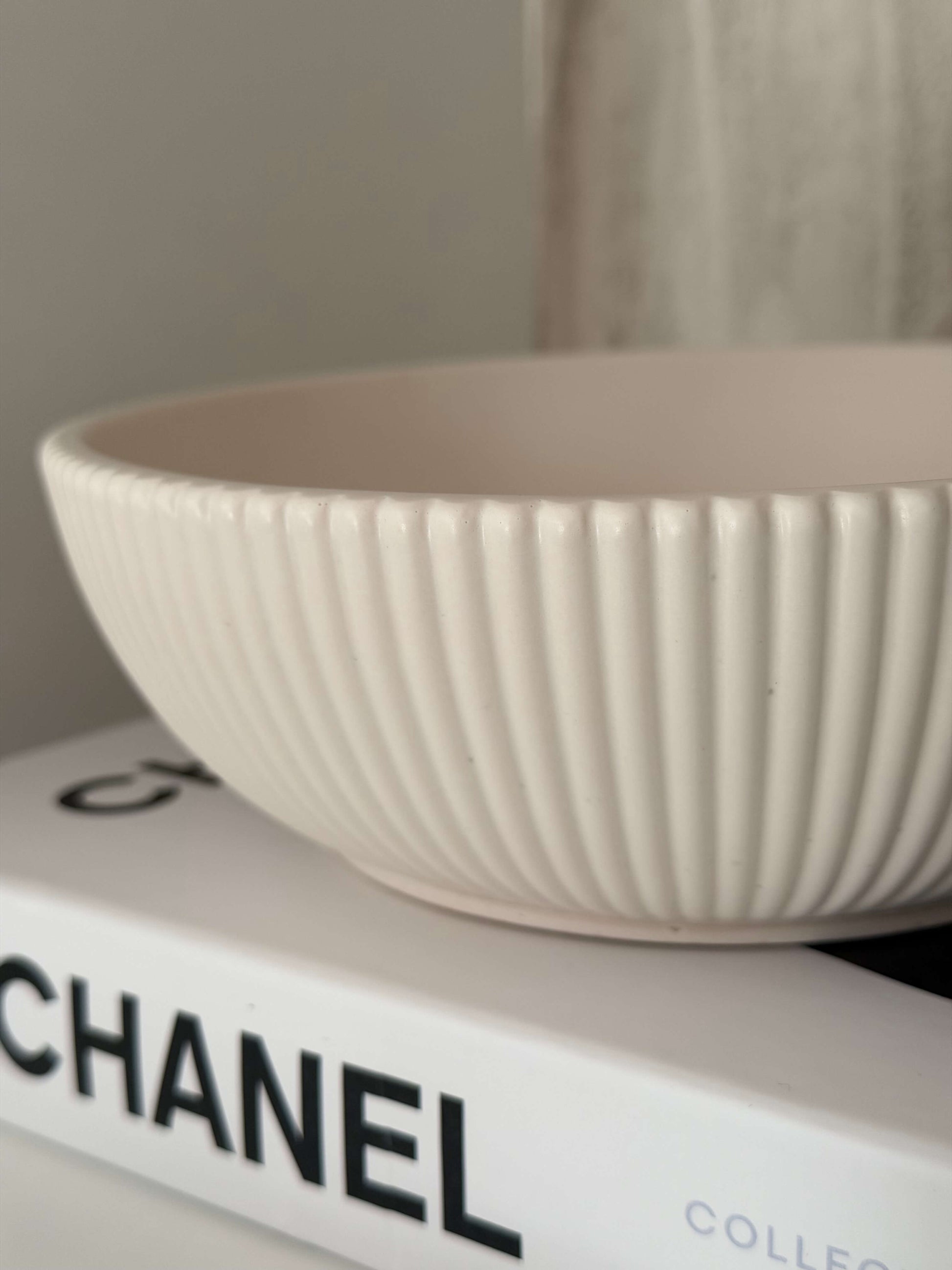 Cremeweiße, handgefertigte Schale mit gerippter Struktur, dekorativ auf einem Chanel-Buch präsentiert
