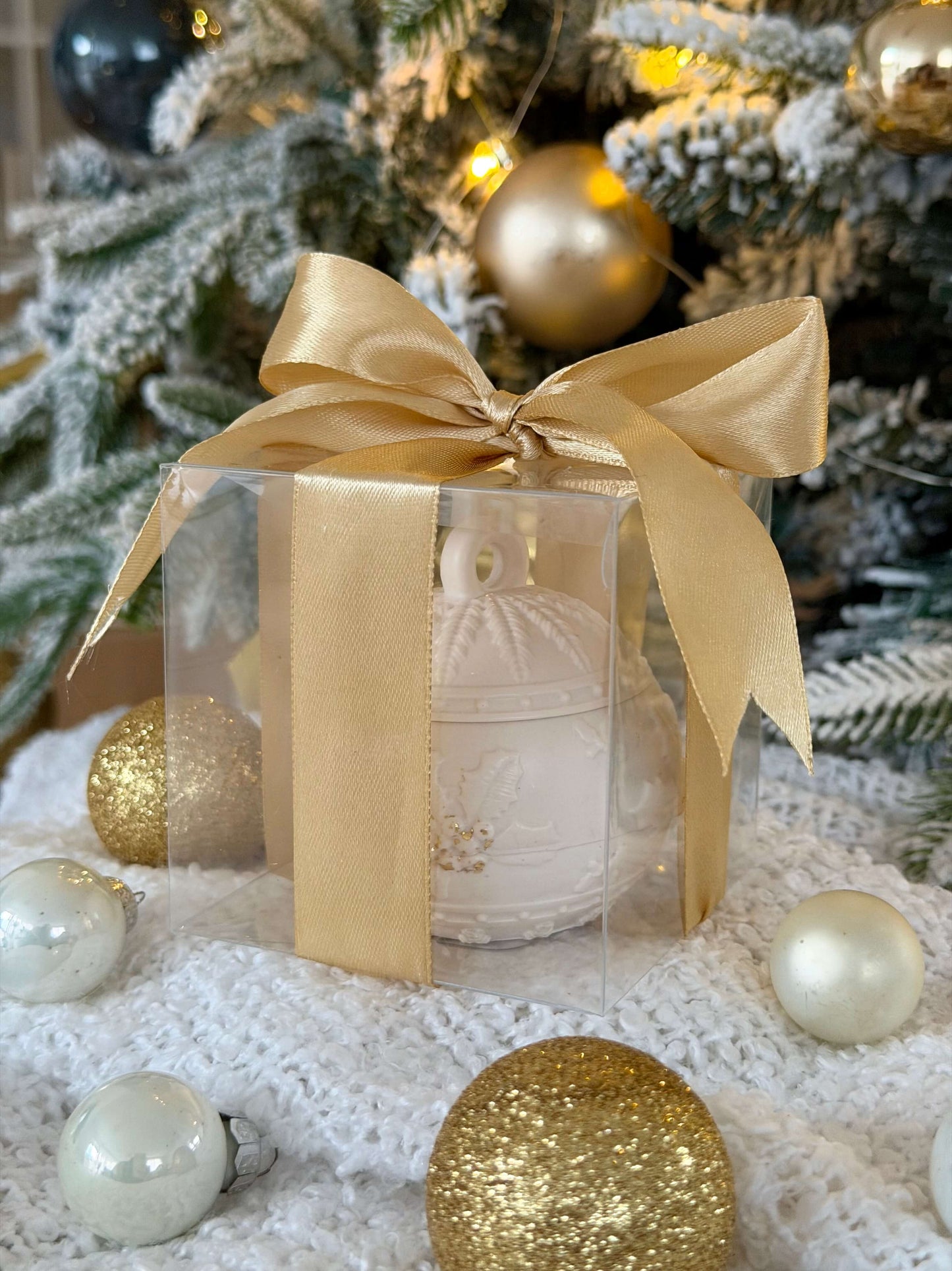 Handgefertigte Weihnachtskugel in transparenter Geschenkbox mit goldener Schleife, dekorativ vor einem festlich geschmückten Weihnachtsbaum präsentiert