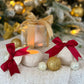 Handgefertigte Weihnachtskugel-Kerzenhalter mit roter Schleife und Geschenkbox, dekorativ mit goldenen Weihnachtskugeln vor einem beleuchteten Weihnachtsbaum arrangiert