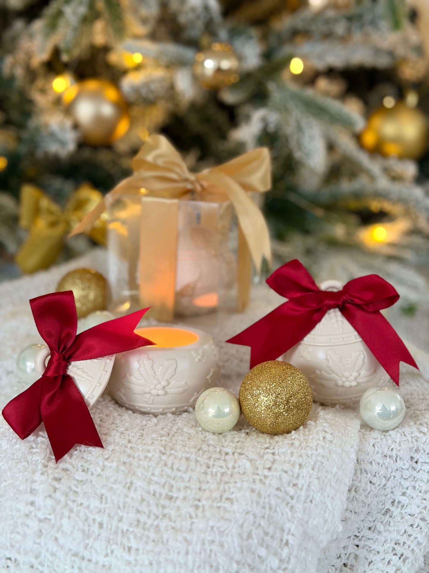 Handgefertigte Weihnachtskugel-Kerzenhalter mit roter Schleife und Geschenkbox, dekorativ mit goldenen Weihnachtskugeln vor einem beleuchteten Weihnachtsbaum arrangiert