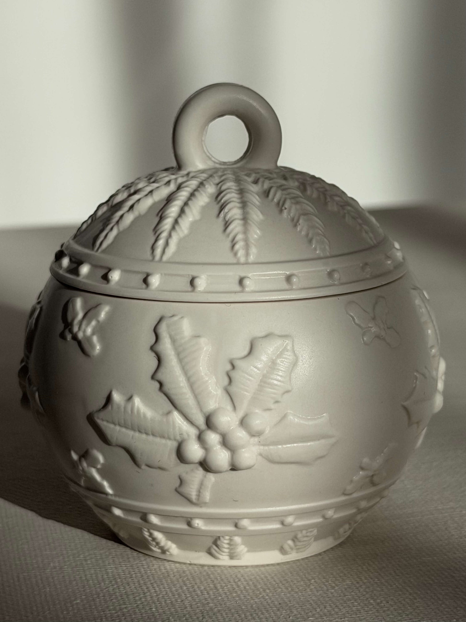 Vorderansicht einer handgefertigten Weihnachtskugel in Weiß mit detailliertem Winterrelief, im sanften natürlichen Licht fotografiert