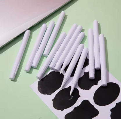 Set aus weißen Kreidemarker mit  schwarzen Etiketten, arrangiert auf grünem Hintergrund – ideal zum Beschriften von Vorratsdosen, Gläsern oder Aufbewahrungsboxen.