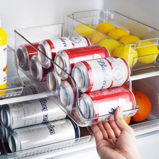 Transparenter Dosenhalter im Kühlschrank, beladen mit rot-weißen Budweiser-Bierdosen und silber-blauen Coors Light-Bierdosen, eine Hand hebt den Halter an. Im Hintergrund sind Zitronen und eine Orange zu sehen.