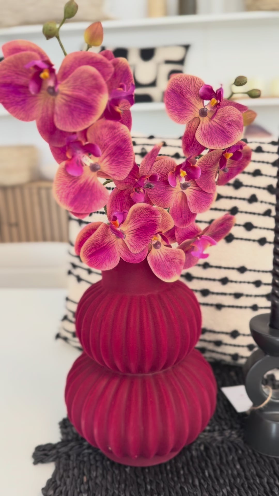 Video die zeigt rote bauchige vase mit Rote Orhudeen,neben hat schwarze Krzenständer und hunten ein schwarz-weiss Kissen.Video zeigt diese arangiment aus verschiedene winkeln