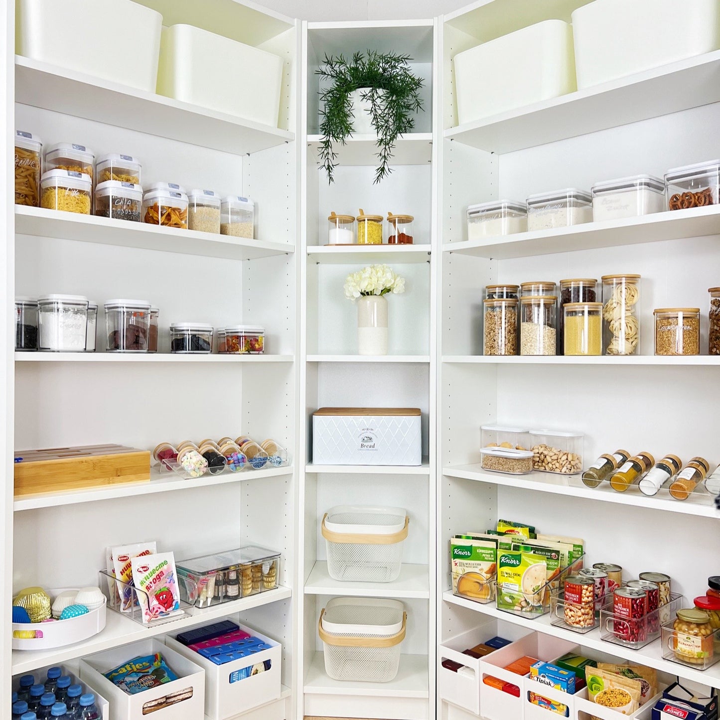 Großzügig organisierte Speisekammer mit stapelbaren Aufbewahrungsboxen, Vorratsdosen aus Glas und Kunststoff, einem Brotkasten und dekorativen Elementen – ideale Lösung für strukturierte Vorratshaltung und Ordnung in der Küche.