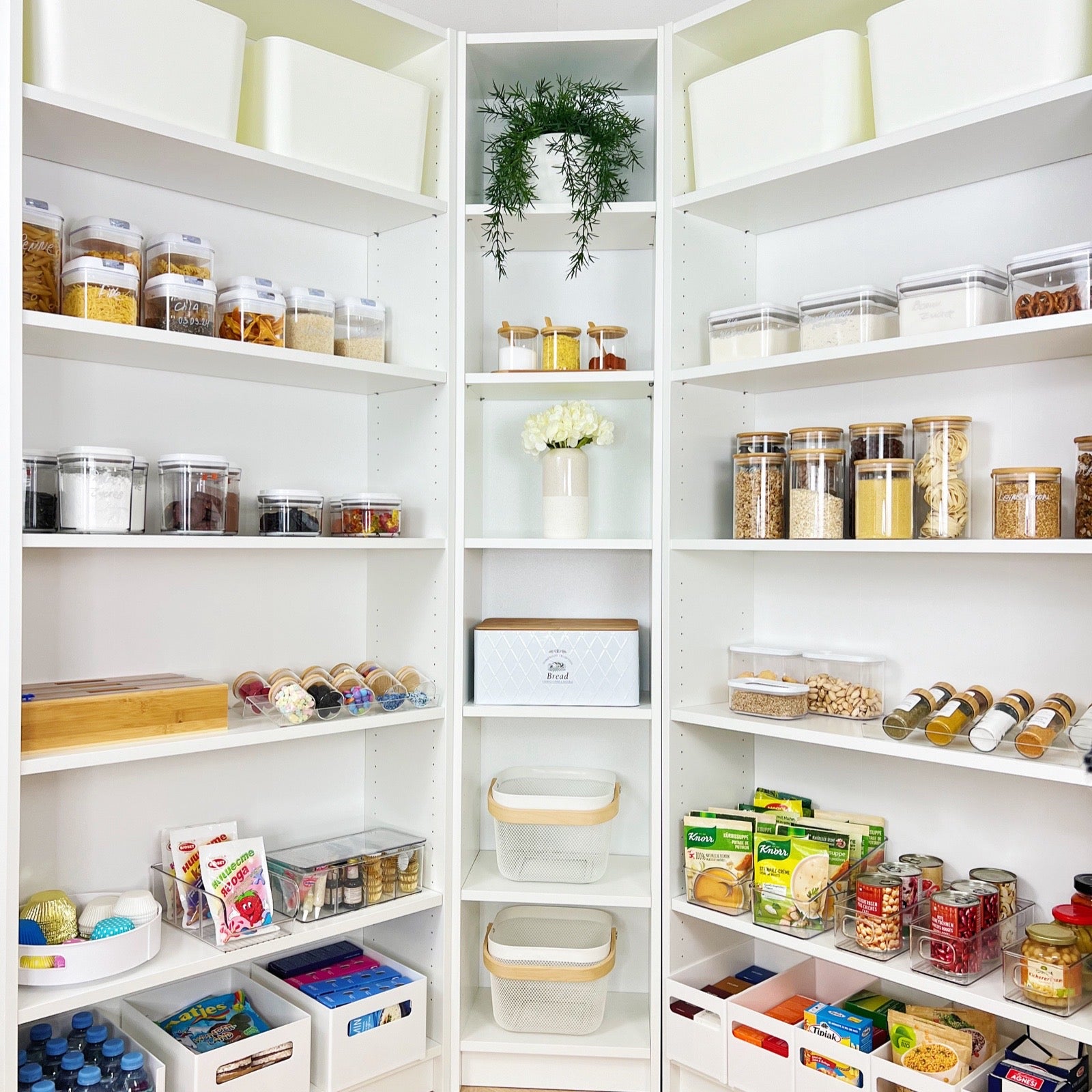 Großzügig organisierte Speisekammer mit stapelbaren Aufbewahrungsboxen, Vorratsdosen aus Glas und Kunststoff, einem Brotkasten und dekorativen Elementen – ideale Lösung für strukturierte Vorratshaltung und Ordnung in der Küche.