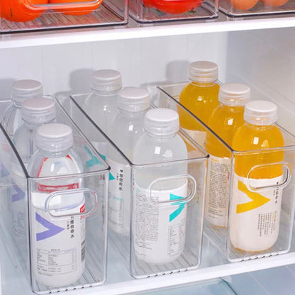 Transparente Aufbewahrungsboxen im Kühlschrank, befüllt mit ordentlich ausgerichteten Wasserflaschen und farbigen Getränken. Die Etiketten der Flaschen sind in verschiedenen Sprachen beschriftet, was auf ein multikulturelles Sortiment hindeutet. Die Boxen ermöglichen eine klare Sichtbarkeit und leichten Zugang zu den Getränken und nutzen den verfügbaren Platz effizient.