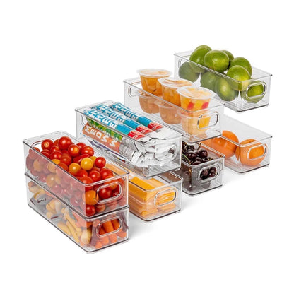 Stapelbare transparente Aufbewahrungsboxen, arrangiert in einer Staffelung, gefüllt mit einer Vielzahl von Lebensmitteln. Zu sehen sind Kirschtomaten, Orangenscheiben, Datteln, Limetten, Wasserflaschen und verpackte Snacks. Die durchsichtigen Boxen sorgen für Übersichtlichkeit und erleichtern die Identifizierung der Inhalte, ideal für die Organisation von Kühlschrank oder Speisekammer.
