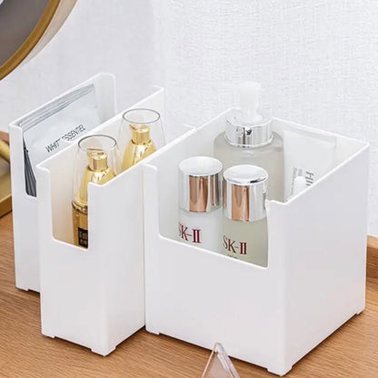 Elegantes, weißes Aufbewahrungssystem auf einer Kommode, bestehend aus zwei halb offenen, stapelbaren Boxen, gefüllt mit hochwertigen Hautpflegeprodukten und Kosmetikartikeln. Links befinden sich Parfumflaschen und ein Magazin, rechts Gesichtscremes und ein Seifenspender, alles übersichtlich angeordnet für einen schnellen Zugriff und eine ansprechende Präsentation von Schönheitsprodukten.